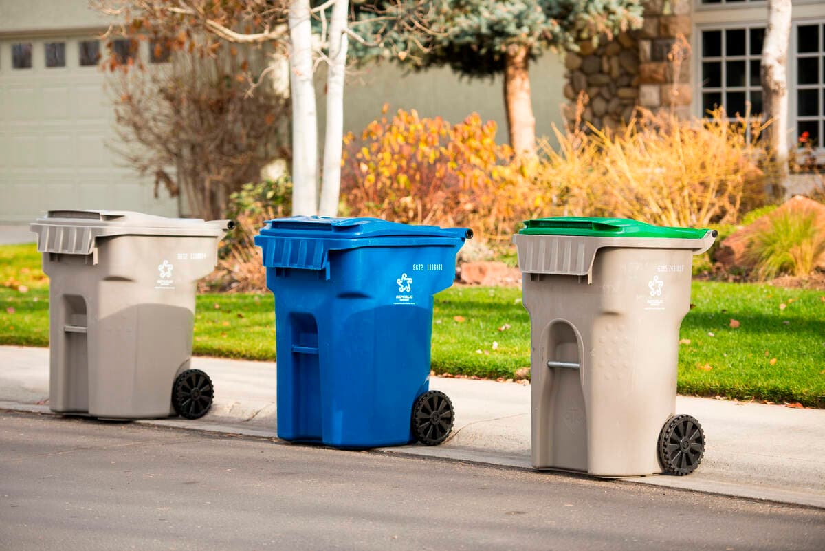 Three trash and recycling bins lined up at the curb in front of a home